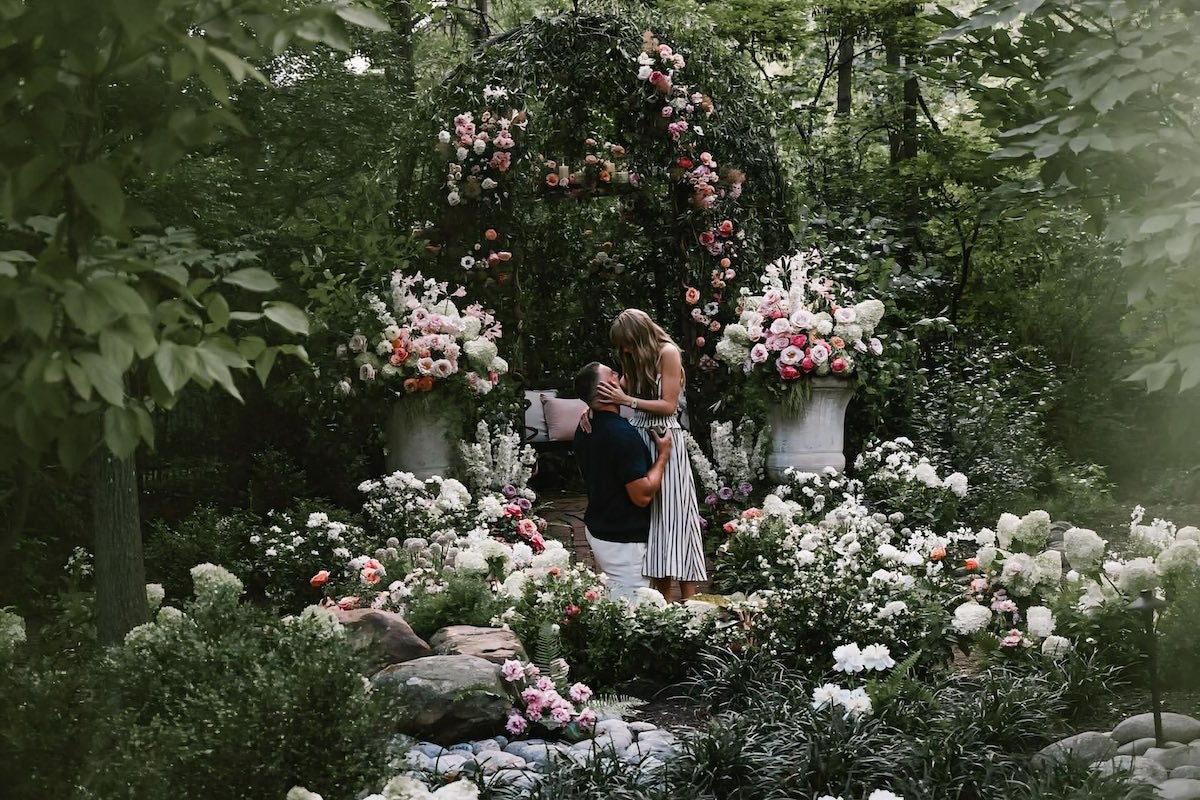 Two people, a man (Kansas City player Travis Kelce) and a woman (Taylor Swift) in a rambling English garden. Kelce is kneeling with his arms around Swift's waist as she holds his face in her hands. Image via Swift/Instagram.
