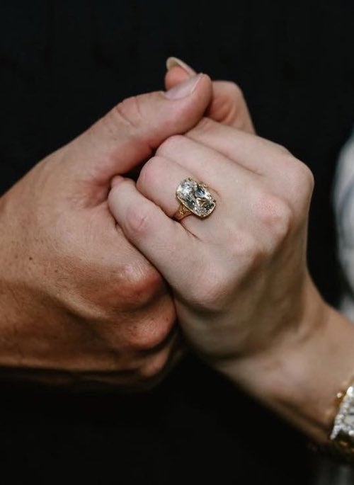 A close of up two hands holding each other, belonging to Kansas City tight end Travis Kelce (left) and singer Taylor Swift (right). On Swift's ring finger, a brilliant and large diamond shines from within a yellow gold band. Image via Swift/Instagram.