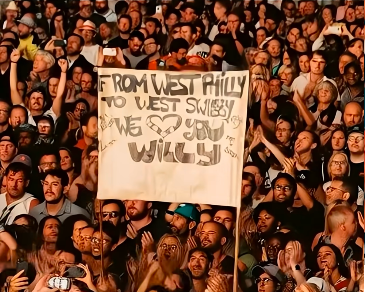 A crowd scene of ghoulish, melted-together faces, with a sign held aloft that says in obviously AI-generated letters "From West Philly to West Swiggy We <3 You Willy"